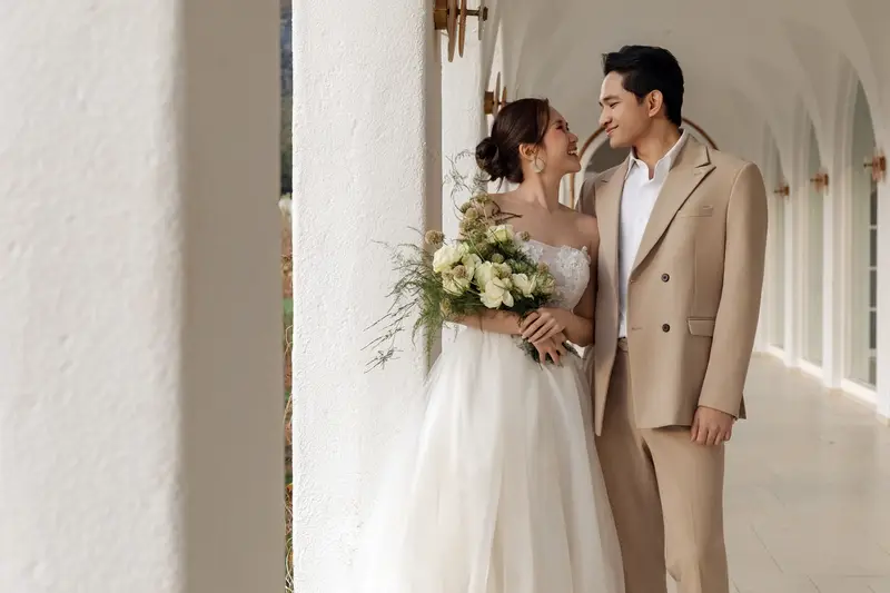 Kia Yuong and Shantanu arm in arm in a white arched colonnade